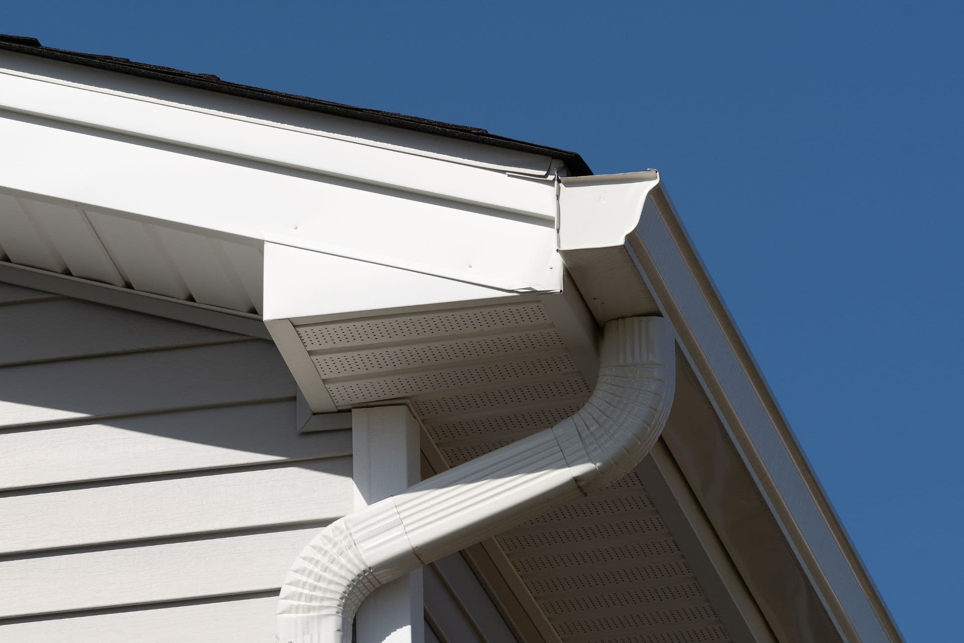 New white gutters and downspout on the corner of a white house.