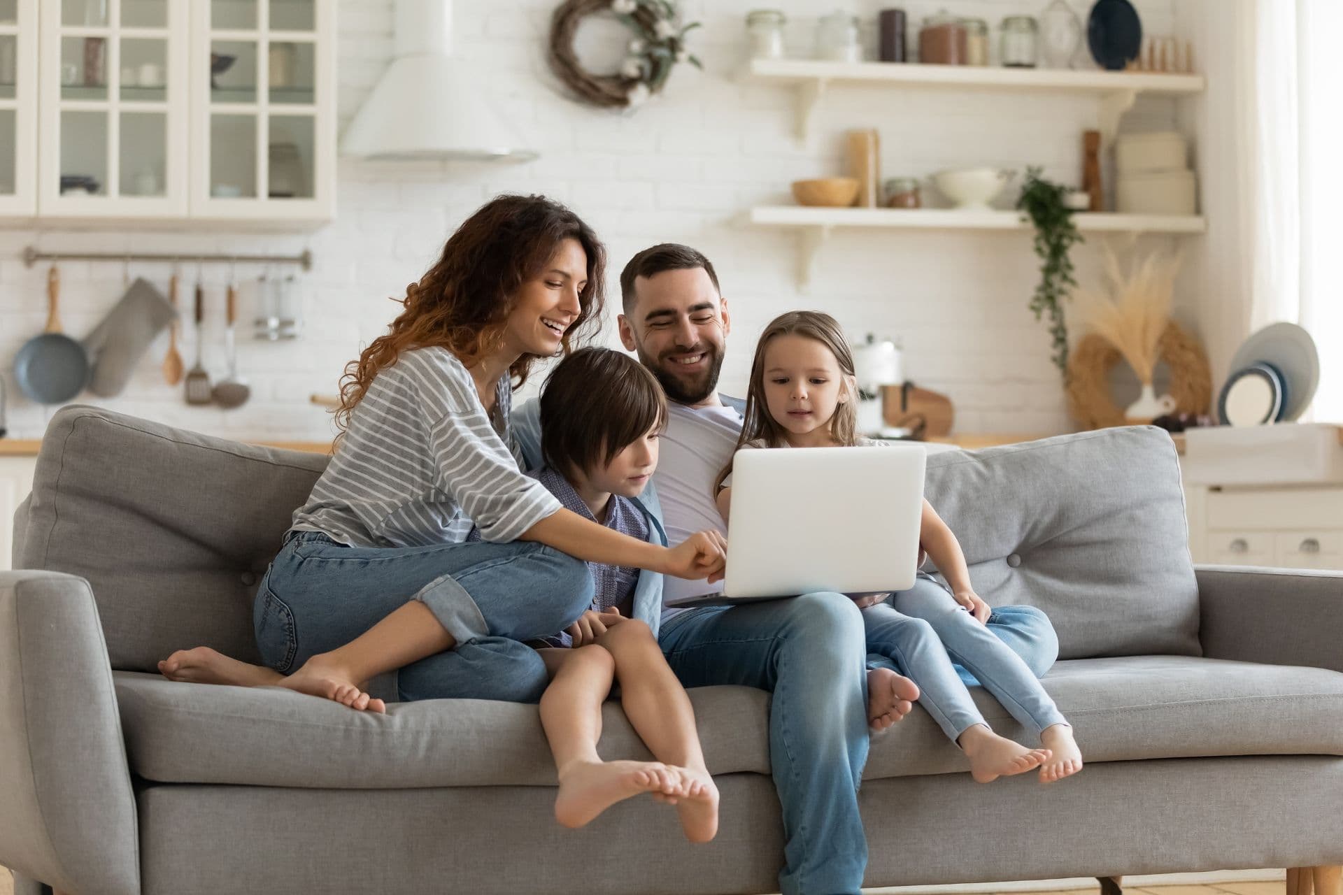 A family sits on a couch crowded around a laptop.