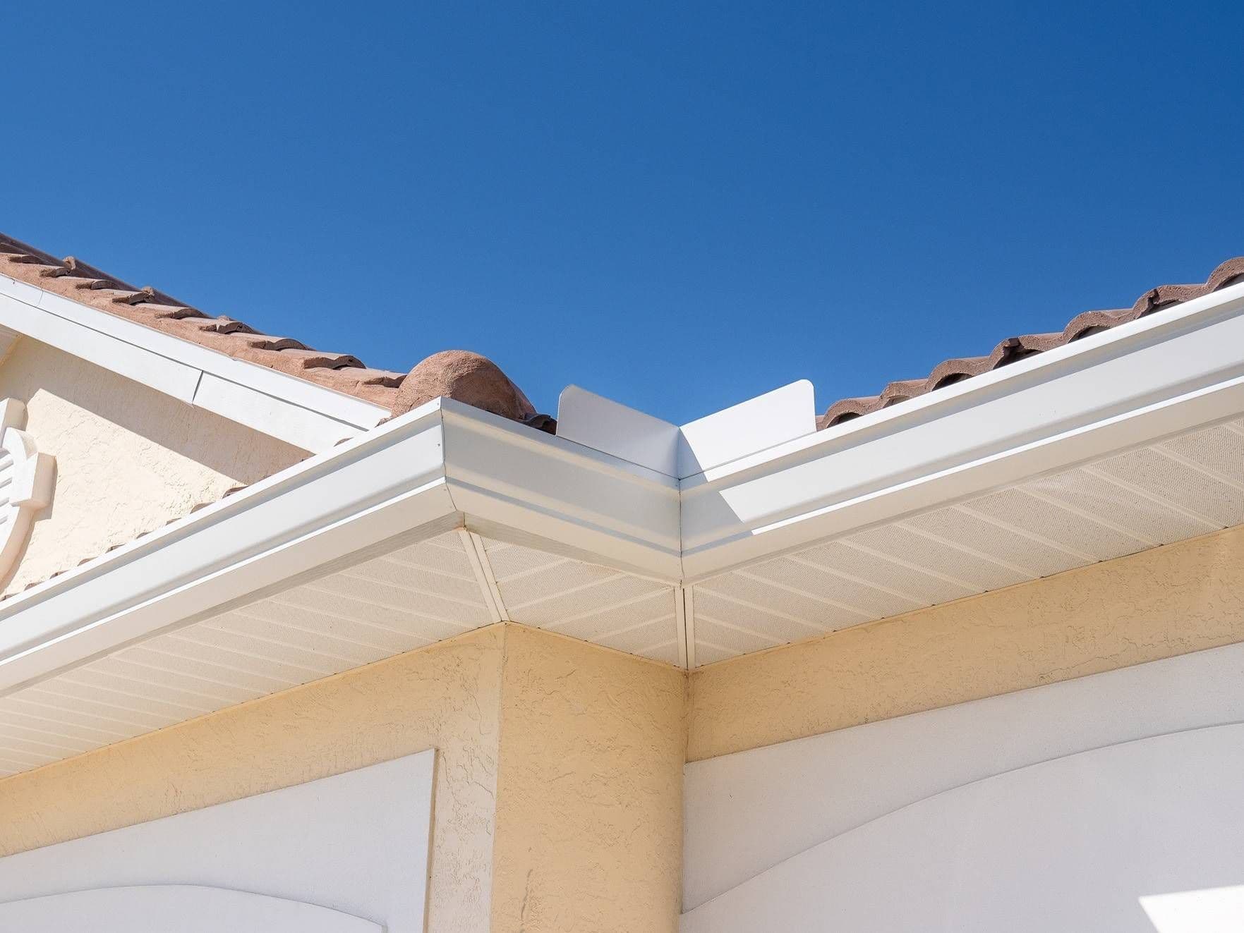 A view of white gutters and soffit on a tan house from below.