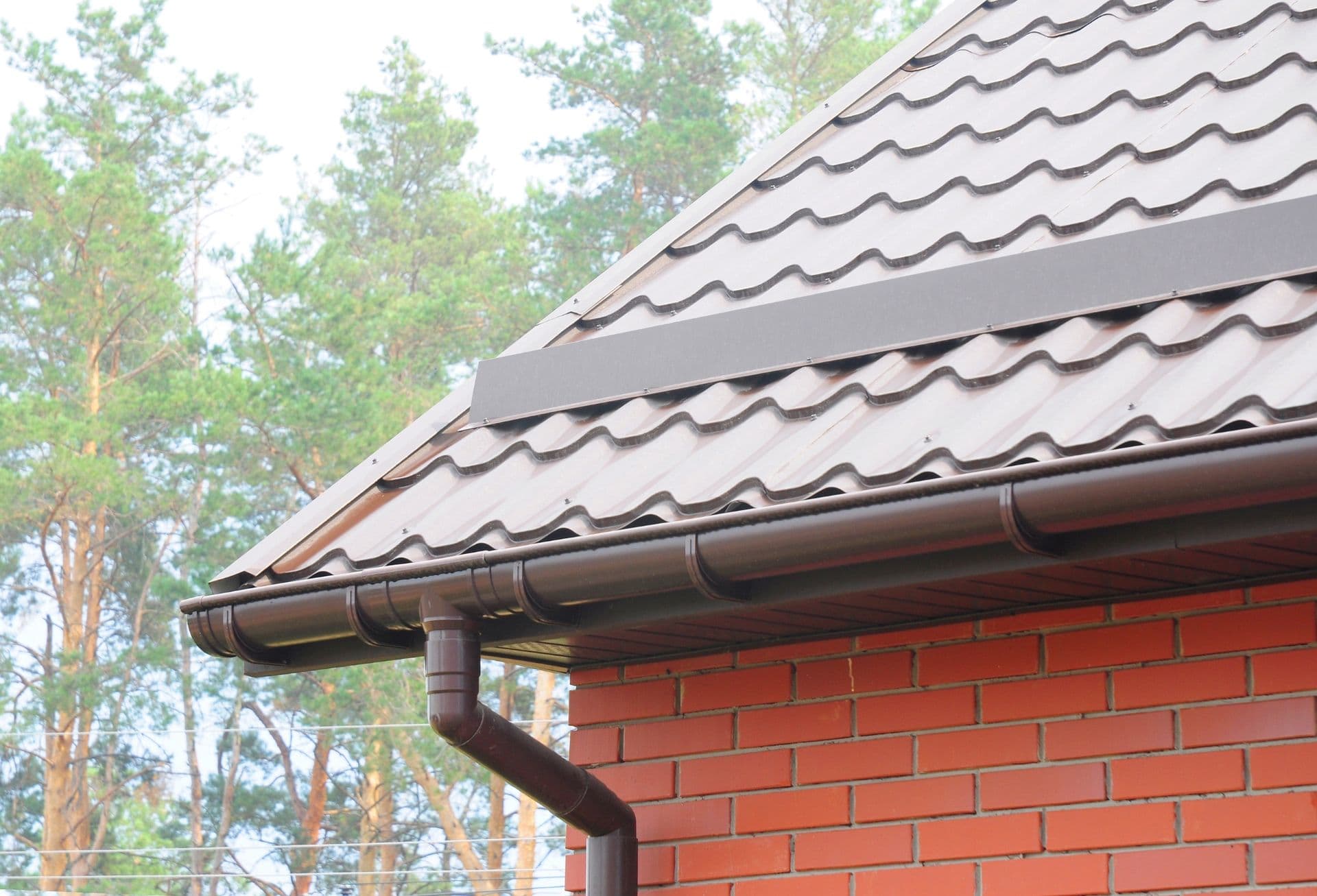 Dark-colored gutters and downspout on a red brick house.