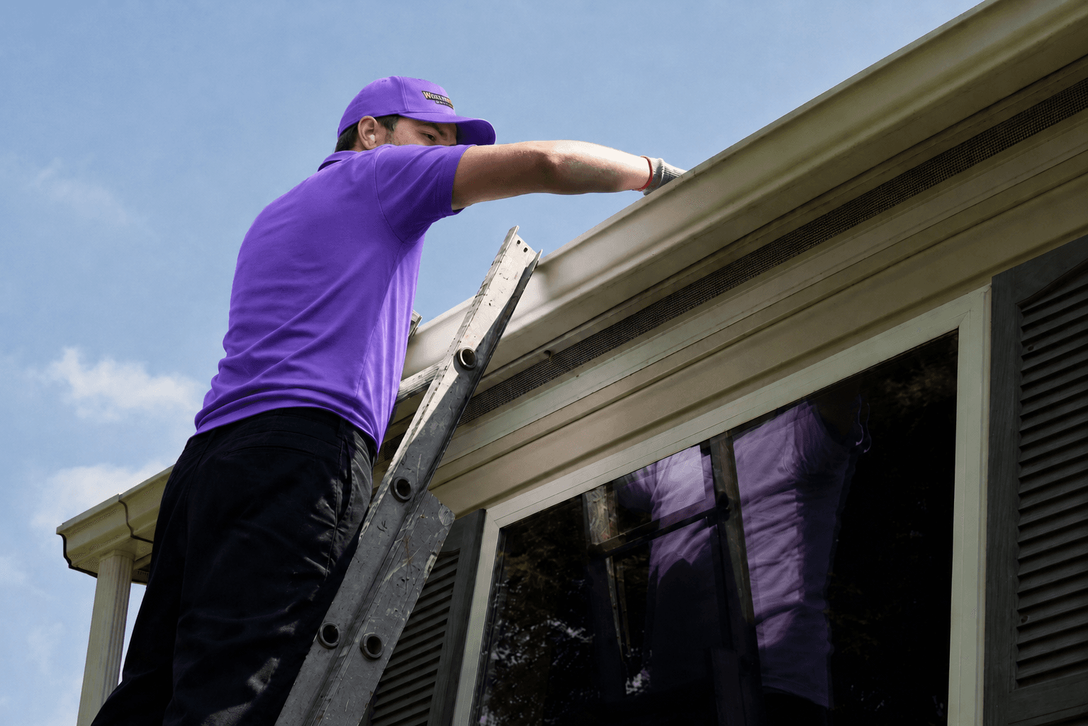 A man on a ladder inspects gutters.